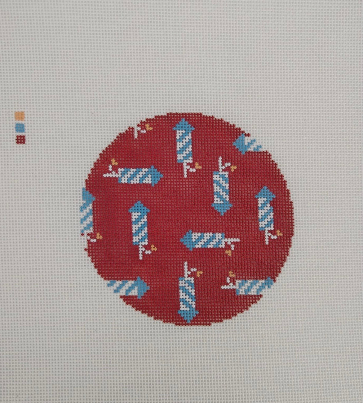 Cross-stitched design of blue and white birds on a red circle with a gray background
